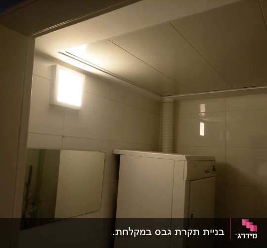 מכונת כביסה בחדר עם קירות גבס ותאורה עליונה